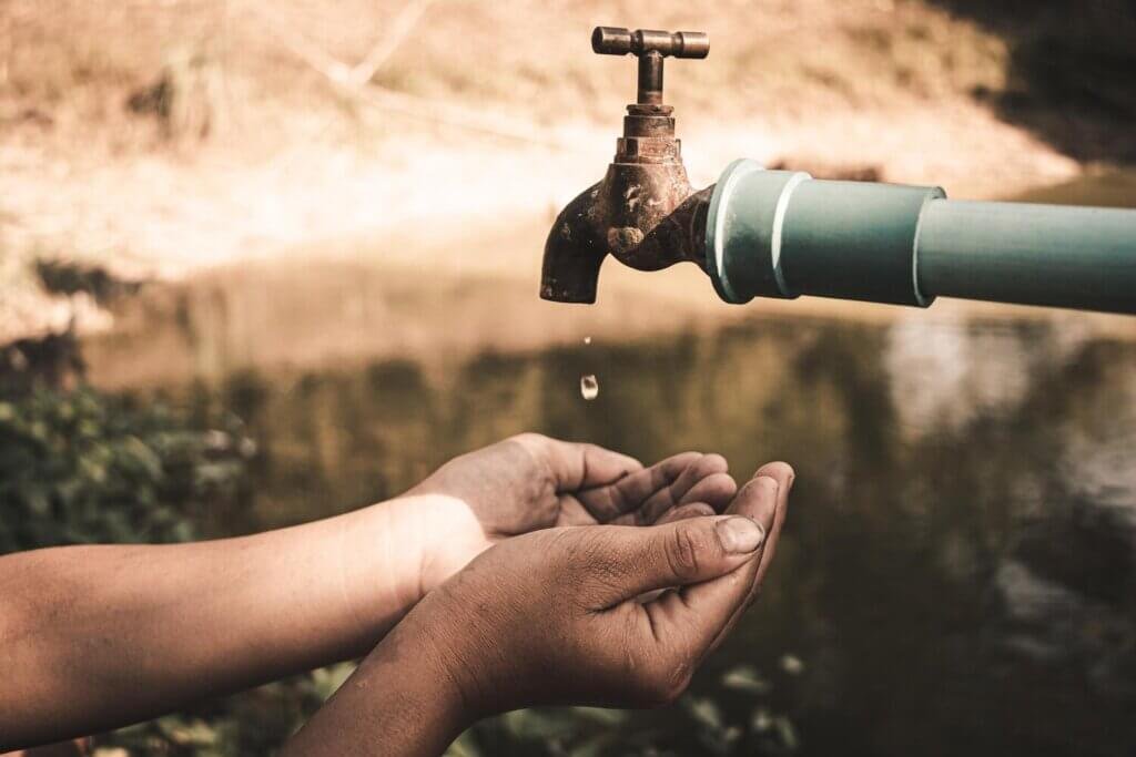 close up hand holding faucet against water 1048944 3222358 racionamento de agua 2